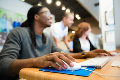 Students in class at computer. Camera is focused on hand/mouse, students in background are blurred
