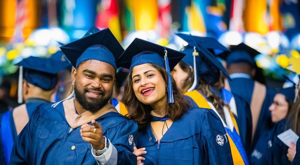 two students at commencement with flags in background
