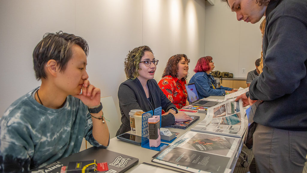 Students sitting with their portfolio books while members of the JWU community look at their designs