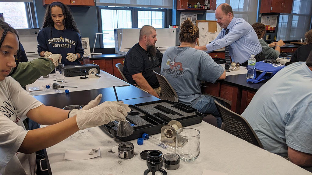 a photo of students and parents at Experience Day using black powder to reveal fingerprints