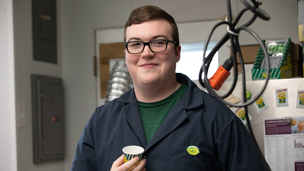 Caleb Atkinson ’24 poses smiling while holding a small tasting cup of Del’s lemonade