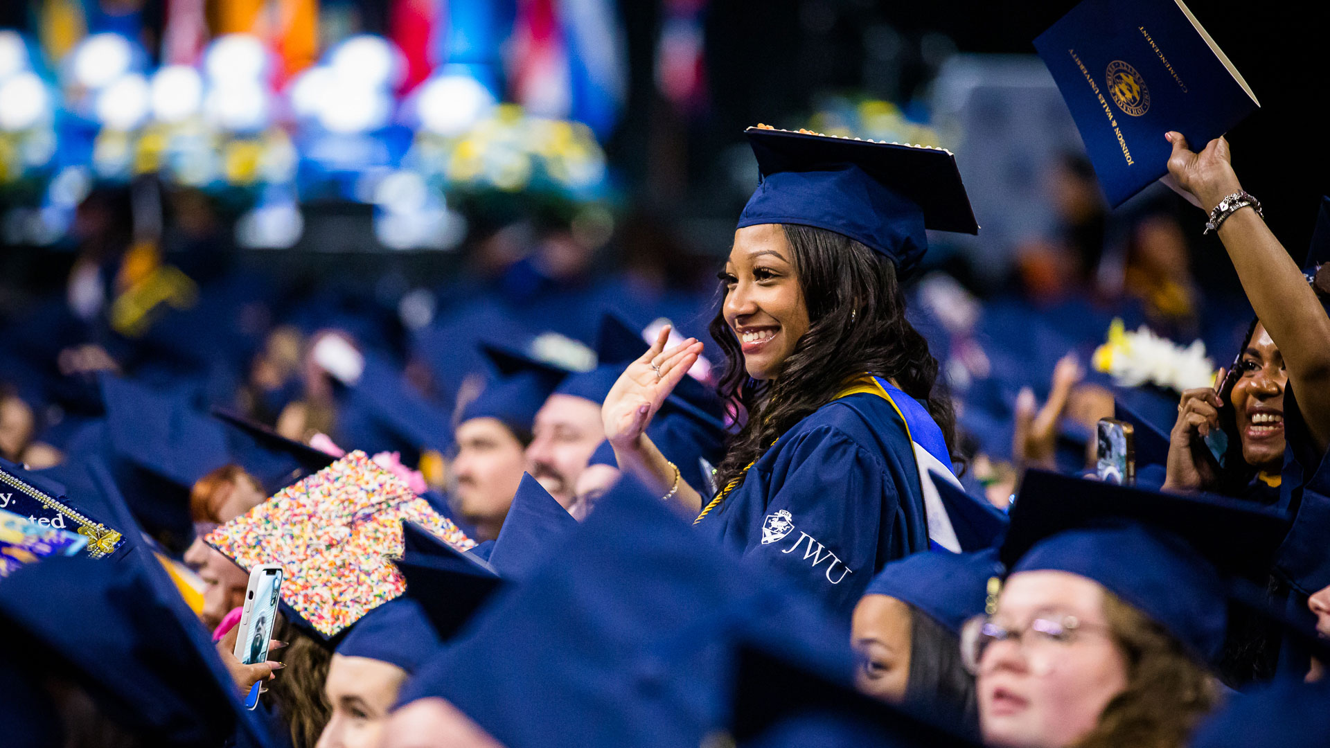 A jubilant grad rises up over the crowd at 2024 JWU Providence Commencement.