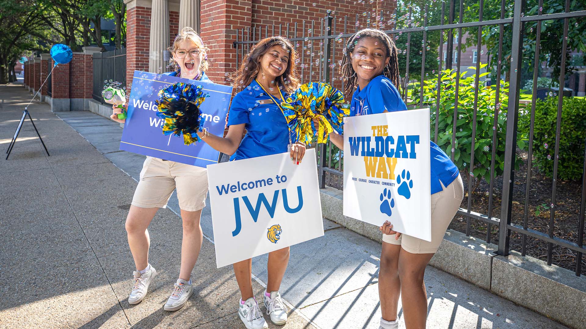 Three girls holding pom poms and signs