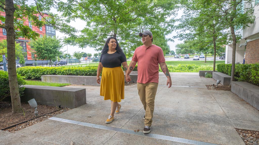 a man and woman walk on campus while holding hands