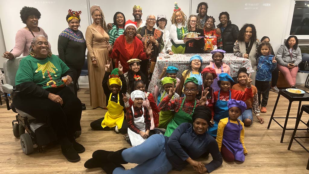 a photo of adults and children groups together, some at a table, some on the floor, while dressed in holiday clothing