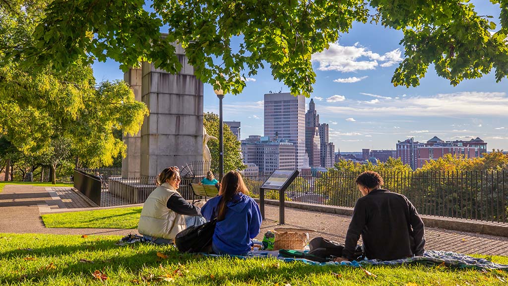 Three people having a picnic in a park overlooking the city of Providence