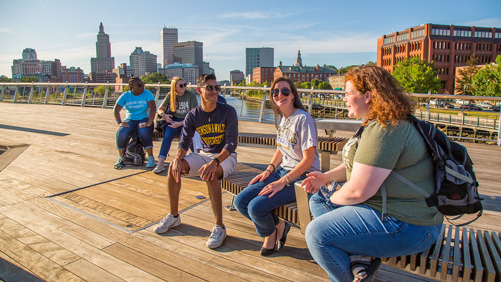 Five students sitting on the pedestrian bridge with Providence in the background