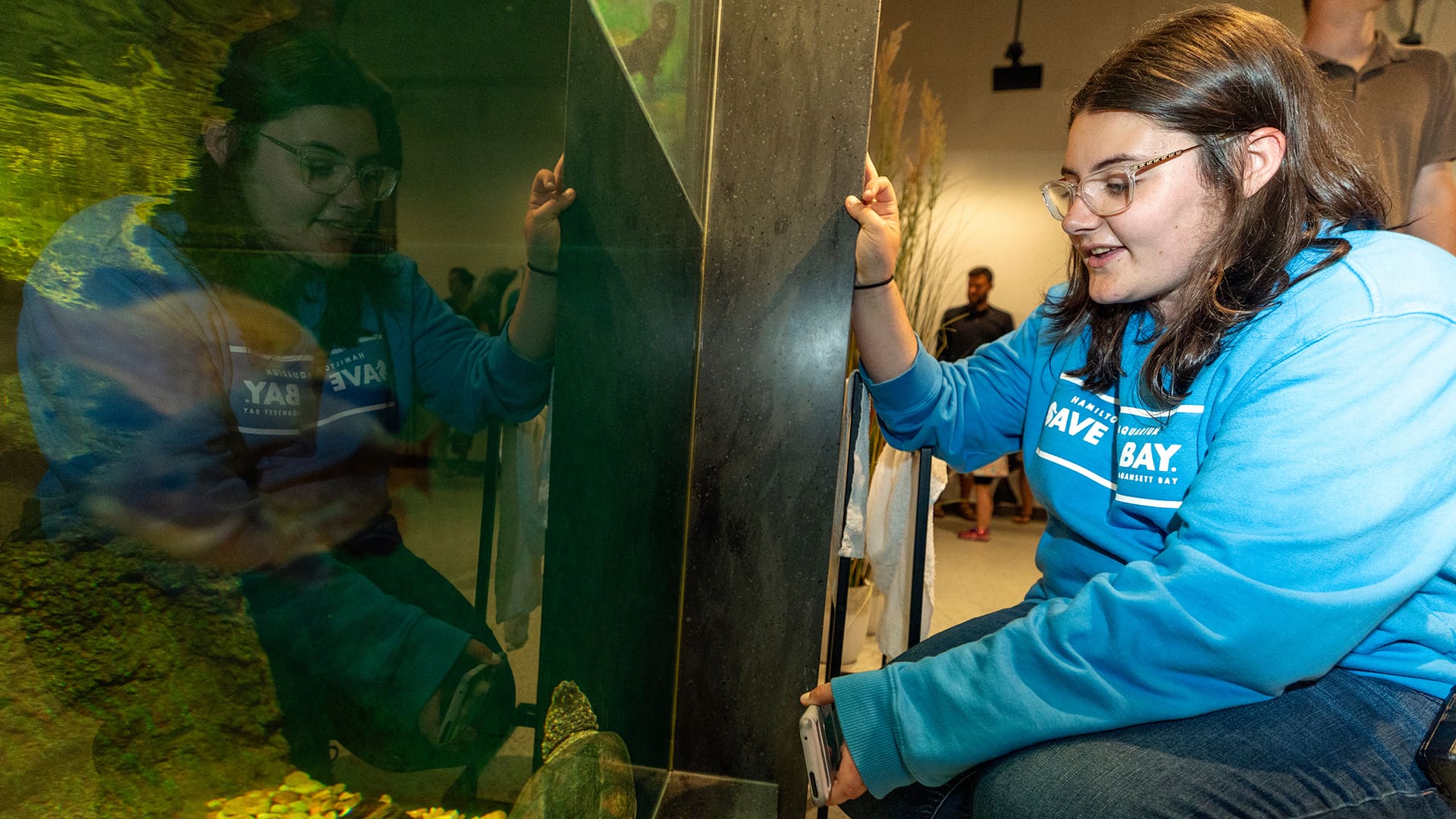 Hailey Sangillo '27 looks at a sea turtle in an aquarium tank; her reflection is clear