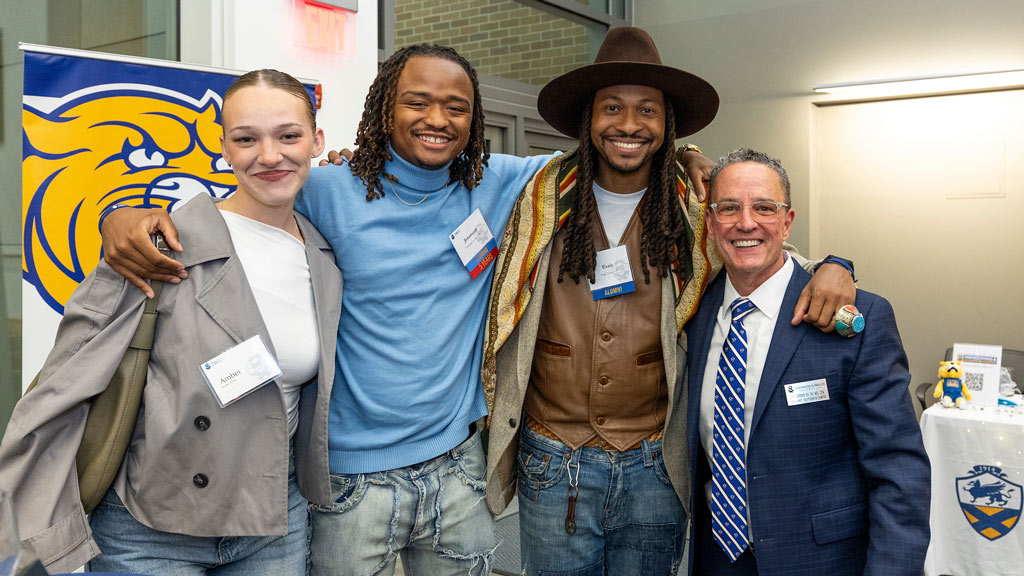 Three alumni pose with president Joseph Greene