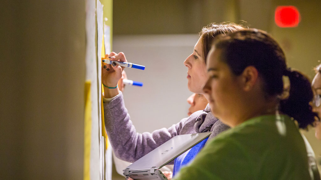 Grad students write notes during a brain-storming session.