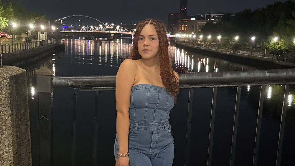 Isabella, a student, posing on a bridge smiling 