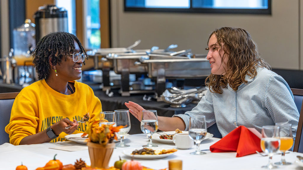 Two female Cross-Country athletes make small talk during the Fall into Fuel luncheon.