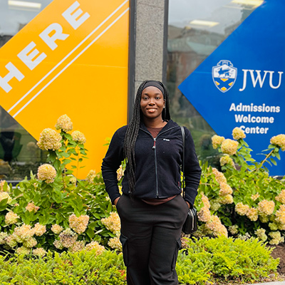 Joy Ilabija '27 MPH poses smiling outside of JWU's Yena Building 