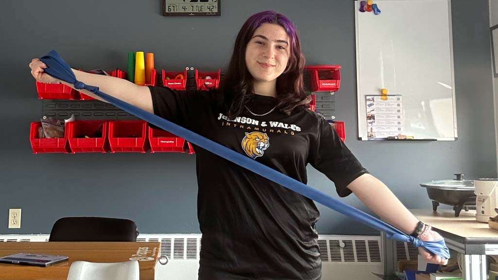 Sofia stretching a resistance band smiling at the camera at her internship